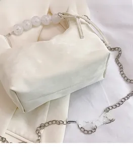Detail of white fabric handbag featuring large pearl beads handle and silver chain strap