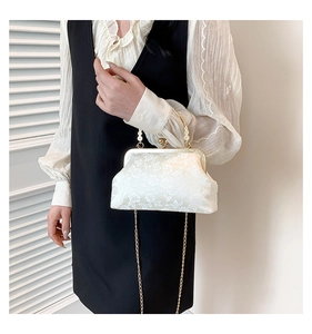 Dettaglio borsa bianca con trama floreale, catena in metallo dorato e chiusura elegante