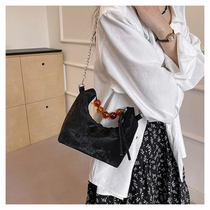Detail of crescent shoulder bag featuring amber beaded handle and silver chain strap