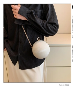 Detail of white marble textured spherical evening bag with elegant gold chain strap