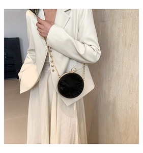 Detail of a black round crossbody bag with gold chain strap on a white blazer