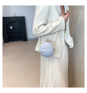 Detail of round spherical clutch bag with wrinkled texture and gold chain on cream suit