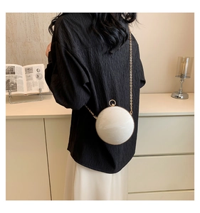 Close-up of circular marble-textured evening bag with gold chain strap on a model