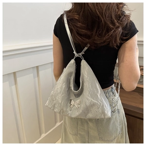 Silver metallic shoulder bag featuring butterfly detail and pleated texture on model