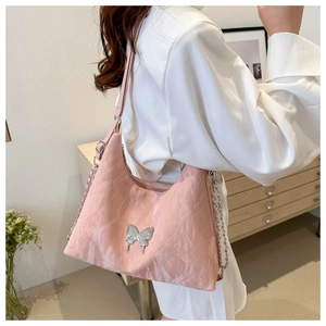 Detail of pink ruched shoulder bag featuring silver butterfly emblem and metal chain