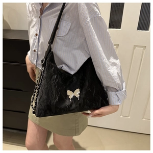 Detail of black wrinkled texture shoulder bag with silver metal butterfly ornament