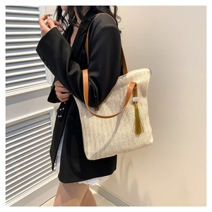 Straw shoulder bag with brown leather handles and gold tassel for spring beach vacation