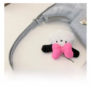 Detail of silver metallic textured crossbody bag with a plush bear charm and pink bow