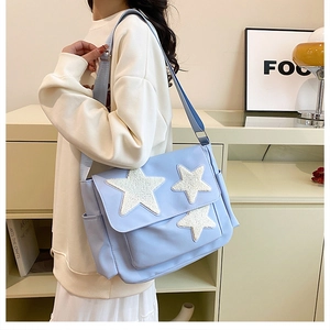 Detail of light blue canvas tote bag featuring plush white star patches and wide strap