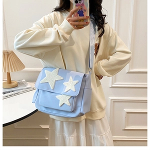 Detail of light blue messenger bag featuring plush white star patches and wide strap