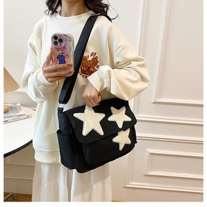 Detail of black canvas messenger bag featuring three white plush star patches on the front