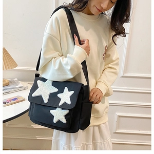 Close-up of black canvas messenger bag featuring three white plush star appliques