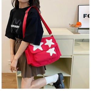 Red canvas messenger bag with white plush stars and adjustable shoulder strap