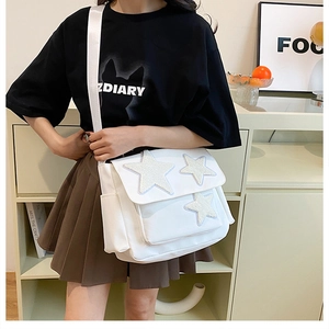 Detail of white canvas crossbody bag featuring plush star patches and wide strap