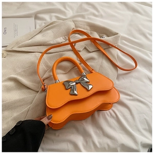 Détail d'un sac bandoulière orange vif avec bord ondulé et nœud en métal argenté