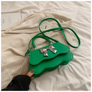 Détail du sac à main vert à bord ondulé avec grand nœud argenté et texture en cuir lisse