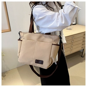 Detail view of a beige canvas tote bag showing contrast brown trim and leather label