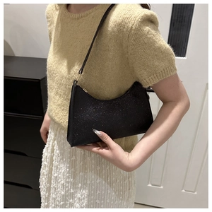 Dettaglio di una borsa baguette con paillettes nere abbinata a un maglione giallo in maglia