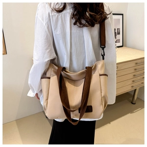 Detailed side view of the beige canvas tote bag showing the dark brown strap and pocket