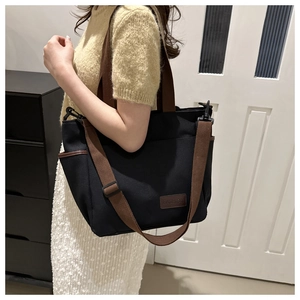 Black canvas tote bag with brown straps and side pockets for casual daily use