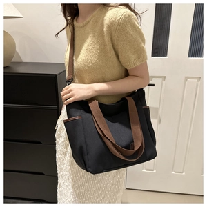 Detail of minimalist black canvas tote with brown woven straps and leather edging