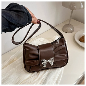 Brown vintage pleated shoulder bag with large bow and silver buckle on white tablecloth