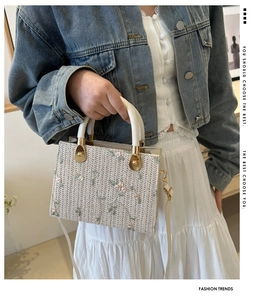 Detail of woven square bag with floral embroidery and white cylindrical top handle