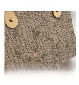 Detail of straw woven bag featuring green leaf and pink flower embroidery with gold clasp