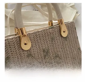 Detailed embroidery of pink flowers and green leaves on a hand-woven straw tote bag
