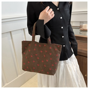 Detail of brown corduroy tote bag featuring red strawberry embroidery with soft handles