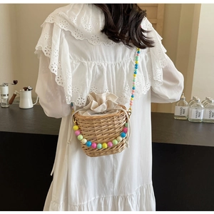 Détail d'un sac seau en paille avec bandoulière en perles colorées et fermeture cordon