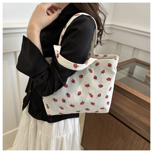 Close-up of white corduroy tote bag with red strawberry patterns on a female model