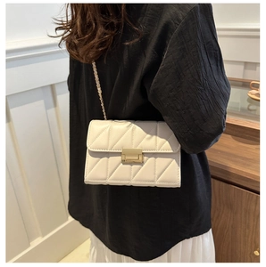 Détail d'un sac bandoulière crème matelassé avec boucle dorée porté par un mannequin