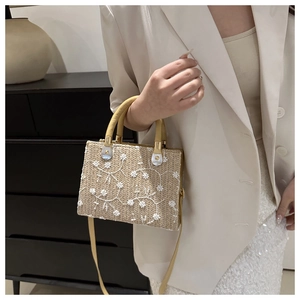 Detail of floral embroidery on a woven straw tote with PU leather straps and gold hardware