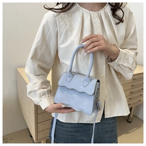 Detail of light blue crossbody bag featuring wavy flap edge and marble print texture