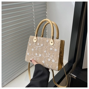 Detailed macro view of lace straw tote bag featuring white floral embroidery and yellow handles