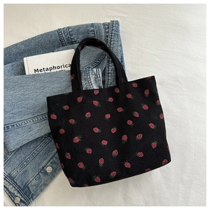 Flat lay of black corduroy strawberry tote bag with denim and book on white linen