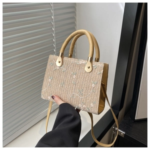 Detailed shot of straw tote bag featuring floral embroidery and leather handles