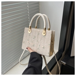 Detail of cream woven square bag with floral embroidery and golden metal hardware