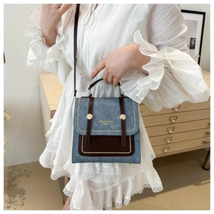 Detail of contrast color crossbody bag with denim blue fabric and brown leather flap