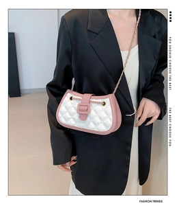 Detail of white quilted crossbody bag with pink contrast trim worn on a black blazer