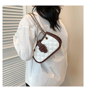 Close-up of white quilted handbag with brown trim and gold chain strap on shoulder