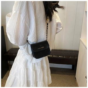 Detail of a black mini crossbody bag with gold chain strap on a white pleated dress