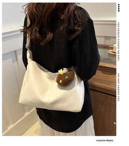 Detail of white PU leather hobo bag with pleated texture and brown plush charm