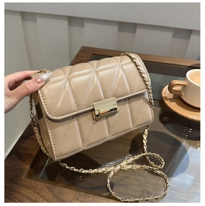 Sac bandoulière beige matelassé avec chaîne dorée et fermoir carré sur table en bois