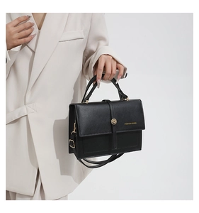 Detail of black leather handbag with metal buckle held by model in cream suit