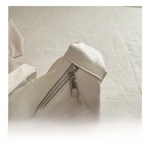 Close-up of smooth silver zipper and lychee pattern leather on cream shoulder bag
