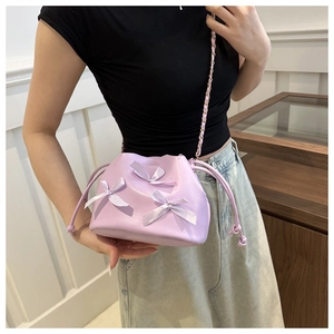 Détail d'un sac seau lavande avec des nœuds en satin et bandoulière chaîne porté par un mannequin