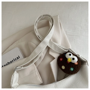 Detail of cream white faux leather tote bag featuring a cute brown plush monster charm