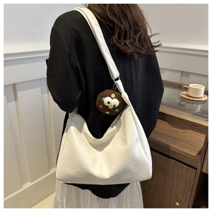 Detail of white lychee texture leather tote bag with a quirky brown plush eye charm